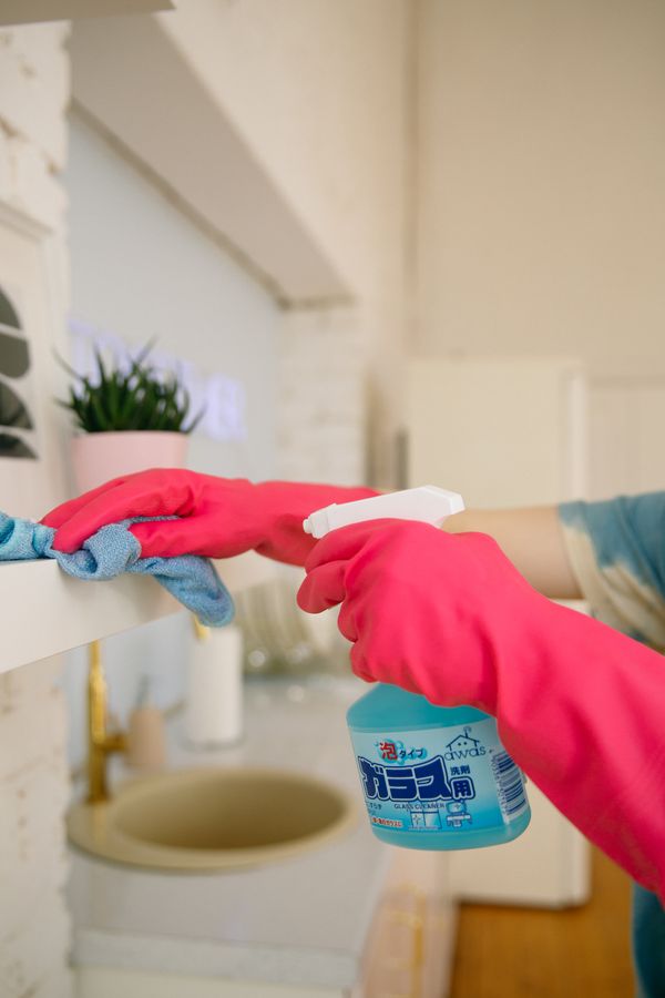 Cleaner in pink gloves wiping a shelf with spray cleaner