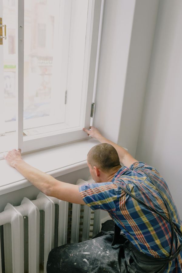 A tradesman fitting a white window frame inside a home