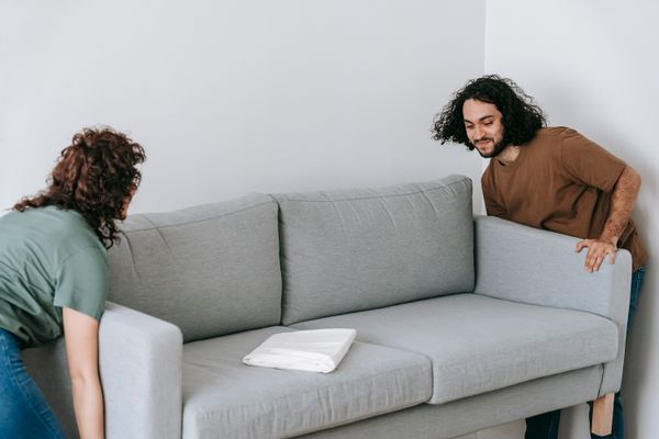 Two people carefully lifting a grey sofa together